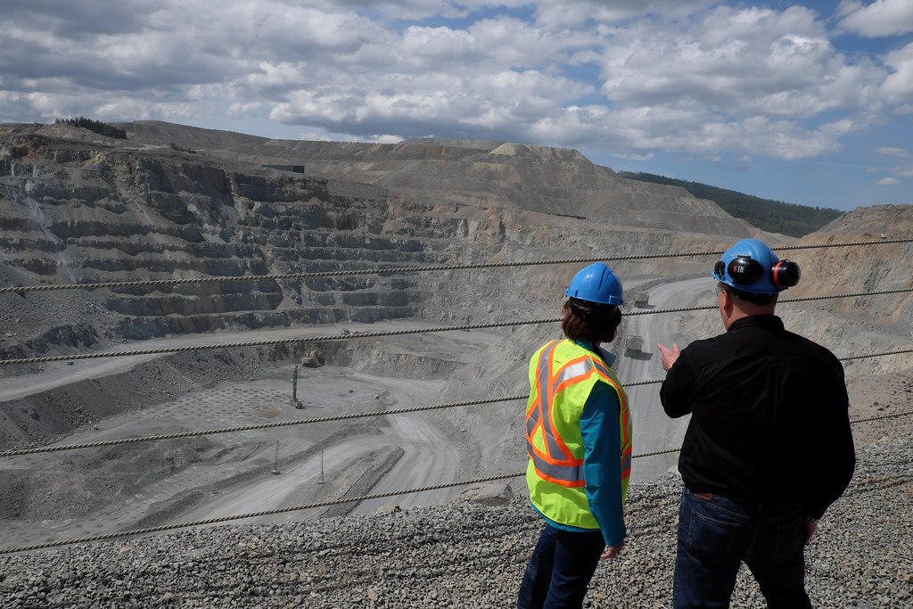 Two mining professionals in hard hats and hi-vis surveying a vast terraced open-pit mine